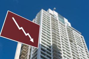 A sign showing an downward arrow in front of a highrise condominium or apartment. Concept of decreasing or slumping condo prices and value or a real estate bust.